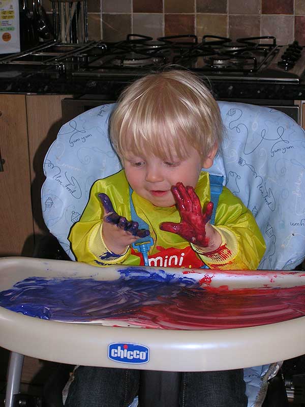 toddler in high chair experimenting with mixing paint colours