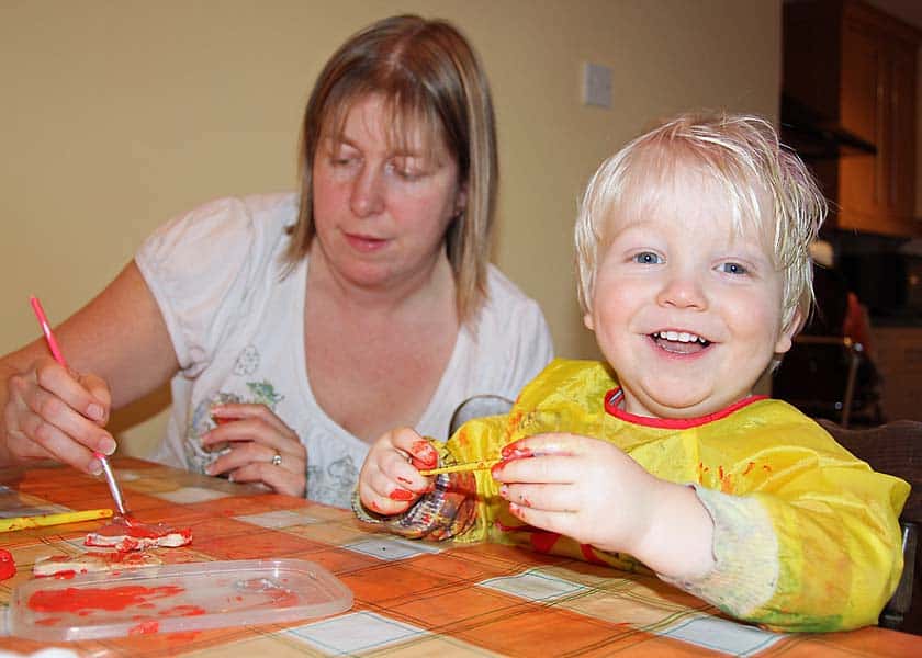 mum joining in with toddler at the kitchen table painting and crafting