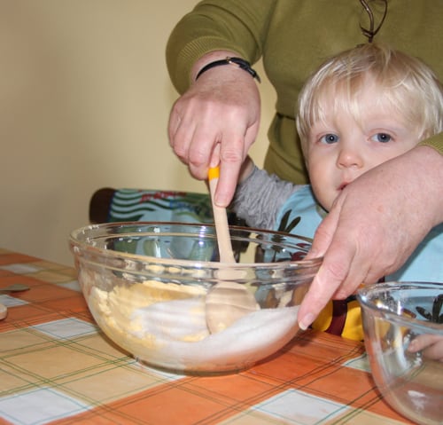 toddler sitting baking with grandma at the table mixing sugar and butter together