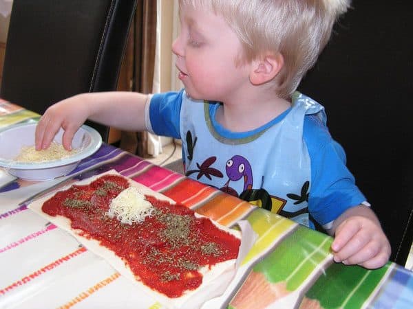toddler sprinkling cheese on pizza