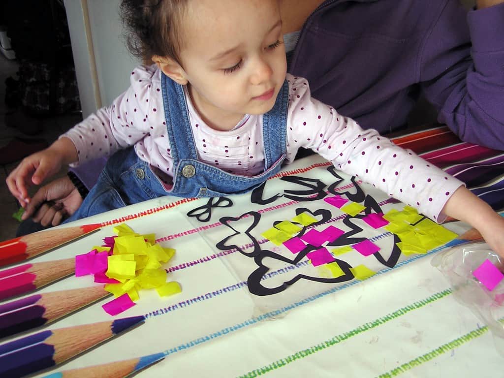 toddler creating a stained glass butterfly picture with black cut out butterflies and pink and yellow tissue paper
