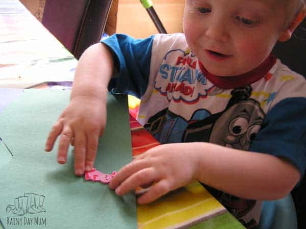 toddler boy putting an animal sticker on a piece of green paper