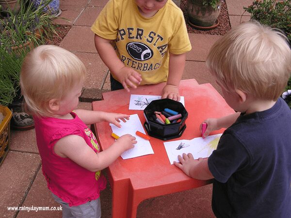 toddlers and preschoolers drawing with crayons and challks at a play table.