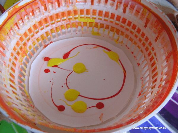 inside of a salad spinner with paints and a paper plate used by toddlers and preschoolers to create a craft for halloween