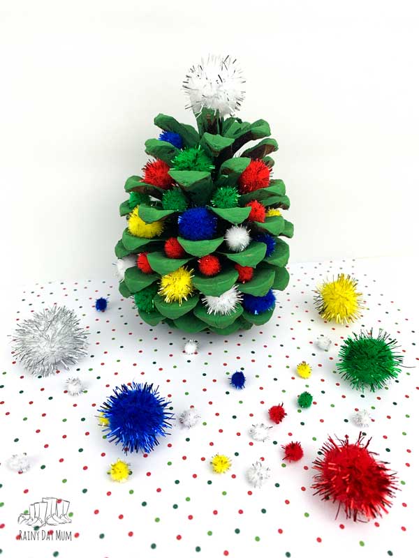 a pine cone Christmas tree painted green and decorated with sparkly pom poms