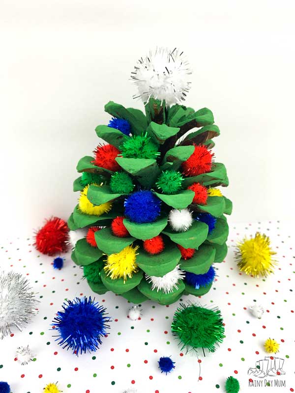a pine cone christmas tree with pom pom decorations made by a child