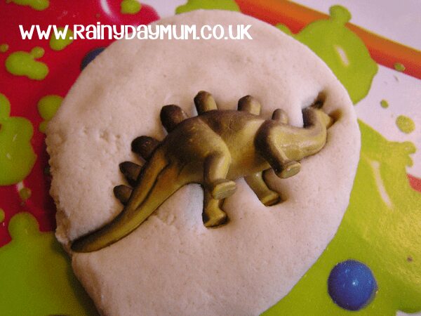 pressing in a toy dinosaur into a salt dough disc to create a fossil