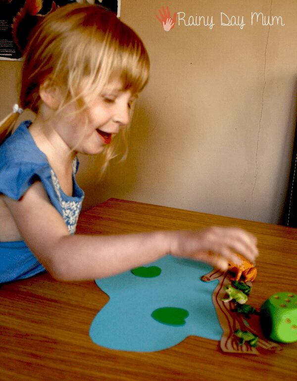 preschool girl counting out the frogs to match the number on the die into the pond.