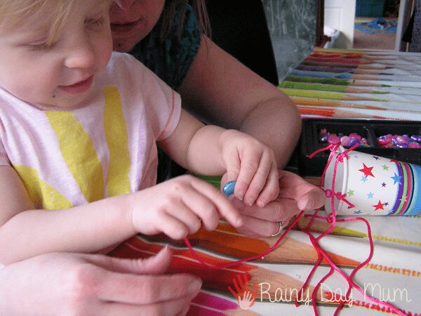 toddler and mum threading beads to create a wind chime from a paper cup