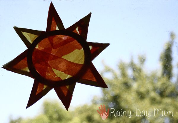 Tissue paper sun, sun catcher created by a toddler on a window sill for summer crafts.