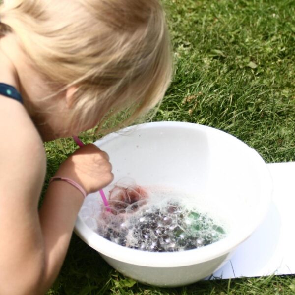 A child creating bubble art in the garden in the summer