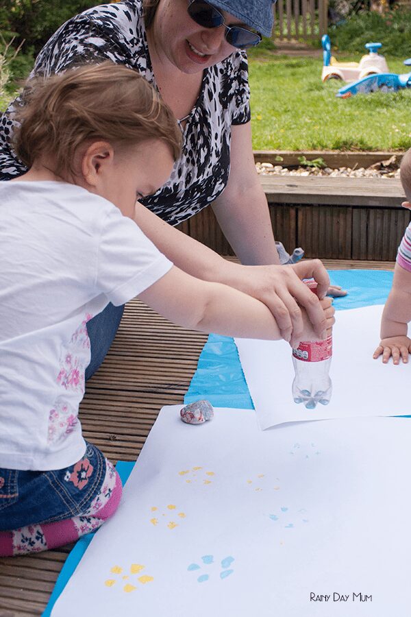 toddler having help from a parent to create prints with a plastic bottle