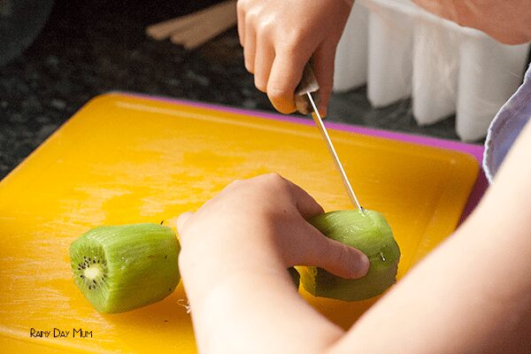 child chopping peeled kiwi fruits on a yellow chopping board.