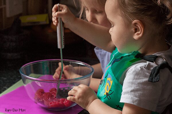 Toddler and preschool squishing fruit with a potato masher to create homemade ice pops for summer.