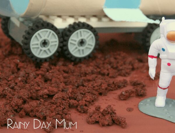 Mars rocks made with red/brown lava rock attached to the surface of cardboard with a kid made Mars rover behind