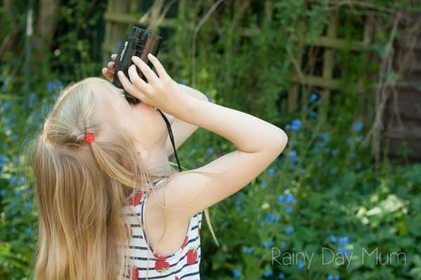 girl using binoculars to view birds in the tree above her.
