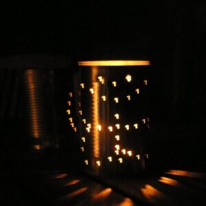 a diy tin can lantern with a butterfly pattern on, there is a candle inside it shining the light through the holes it is set on a table and in the dark on a summer's evening