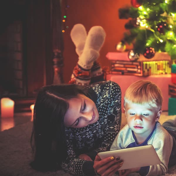 child and mum by the Christmas tree looking at movies on a tablet