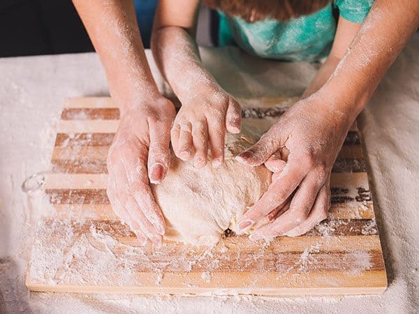 child and parent kneading bread dough on a wooden chopping board