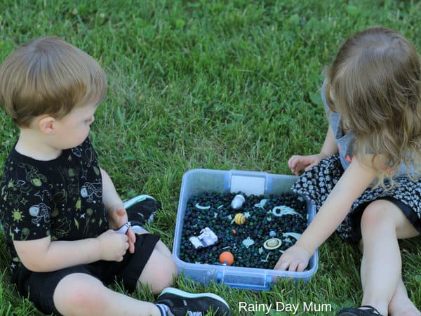 siblings playing with simple sensory bin with a space theme