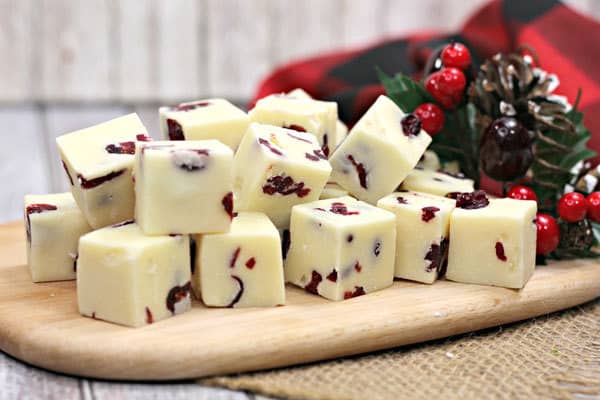 Christmas fudge recipe made with White Chocolate and Cranberries displayed on a wood chopping board with Christmas Decorations in the background