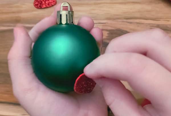 adding a foam heart to a bauble to create an easy christmas craft with toddlers making grinch inspired christmas baubles for the tree