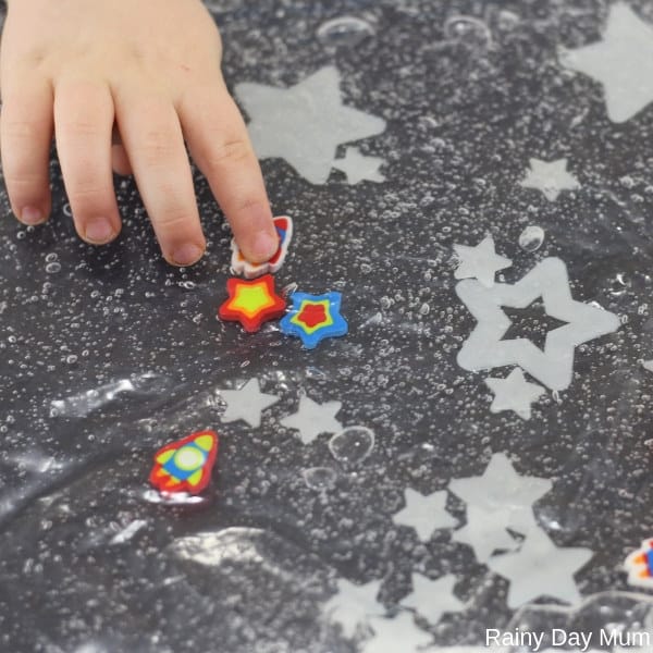 toddler playing with a glow in the dark space themed sensory bag taking the rocket to the different sized stars