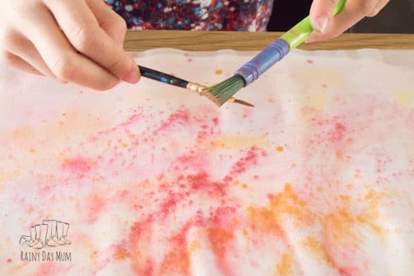 splattering using 2 paintbrushes onto a wet painting