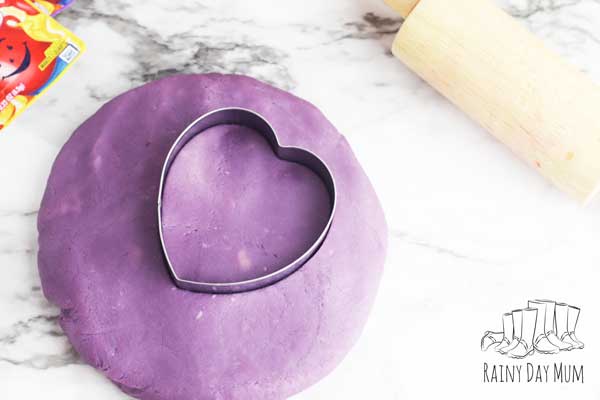 grape kool-aid play doh on a marble background with a cookie cutter heart and rolling pin