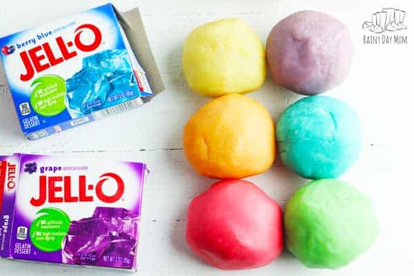 balls of colourful play dough made with jell-o alongside 2 boxes of the jell-o
