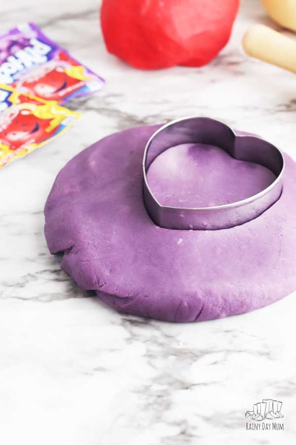 purple grape kool-aid playdough with a heart cookie cutter and red ball of cherry playdough above