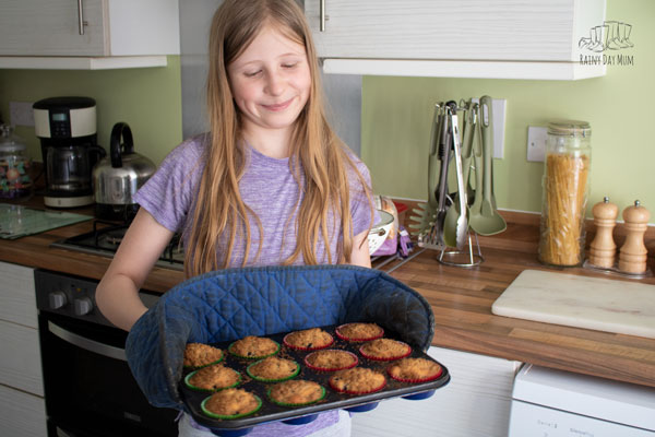 child holding a tray of blackberry muffins straight from the oven