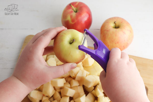 child peeling apples over a wooden chopping board