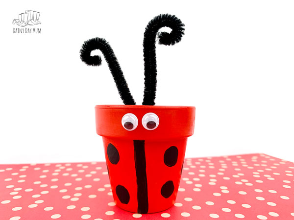 clay pot ladybug craft finished with pipe cleaner antenae on a red spotted paper against a white background
