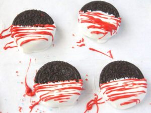 4 Oreos half covered in white candy melt on parchment paper with red candy melt drizzled over them in strippes