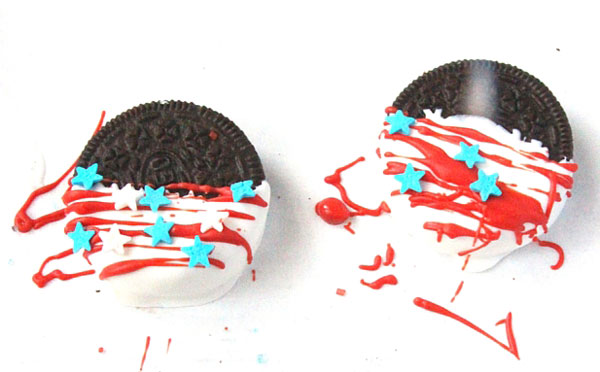 2 Oreo Cookies half dipped in white candy melts with red stripes drizzled on and blue and white star sprinkles placed on top drying on white parchment paper