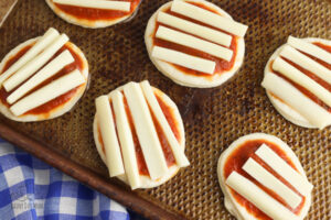 adding string cheese to mini pizzas that are so simple kids can cook themselves, there are 6 of these on a baking tray