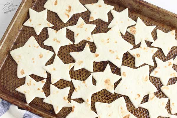 multiple sizes of star shaped tortilla chips on a baking tray sprayed with cooking spray