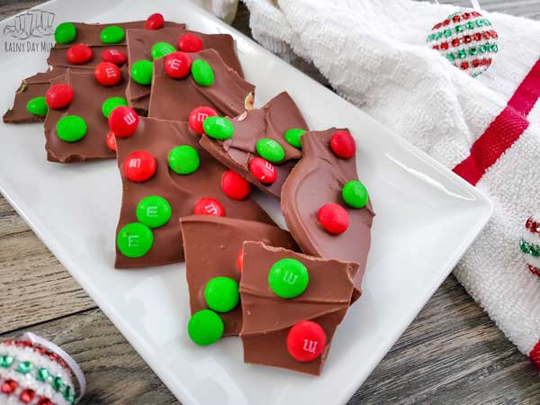 christmas chocolate bark with red and green m&ms dotted on the surface on a wooden table