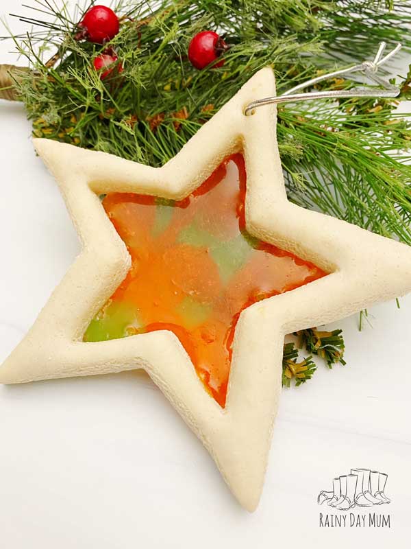 Christmas star salt dough ornament with an orange and green stained glass centre on the branch of a Christmas tree