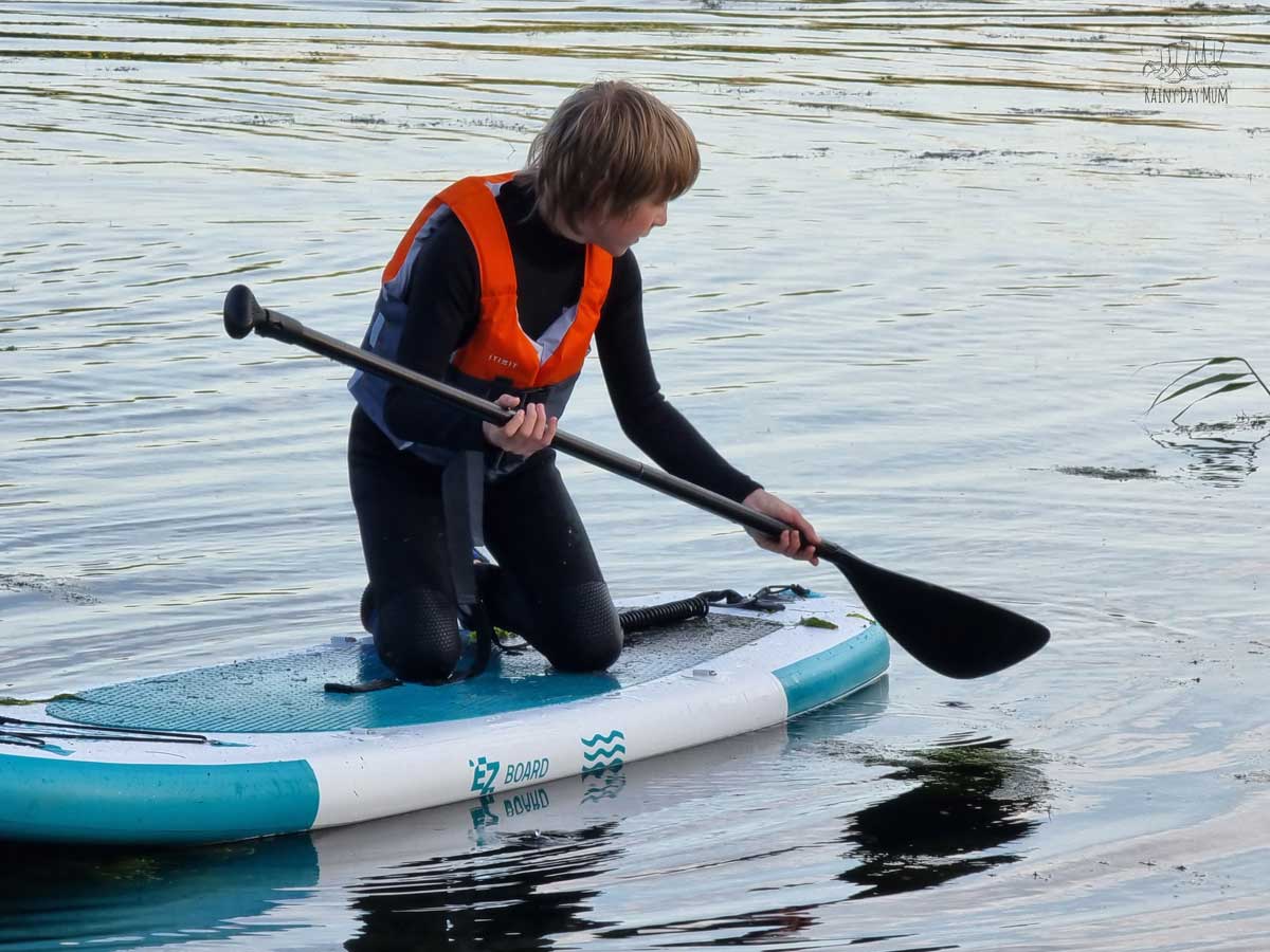 A tween holding the paddle of the EZ Kids Paddleboard in the water.