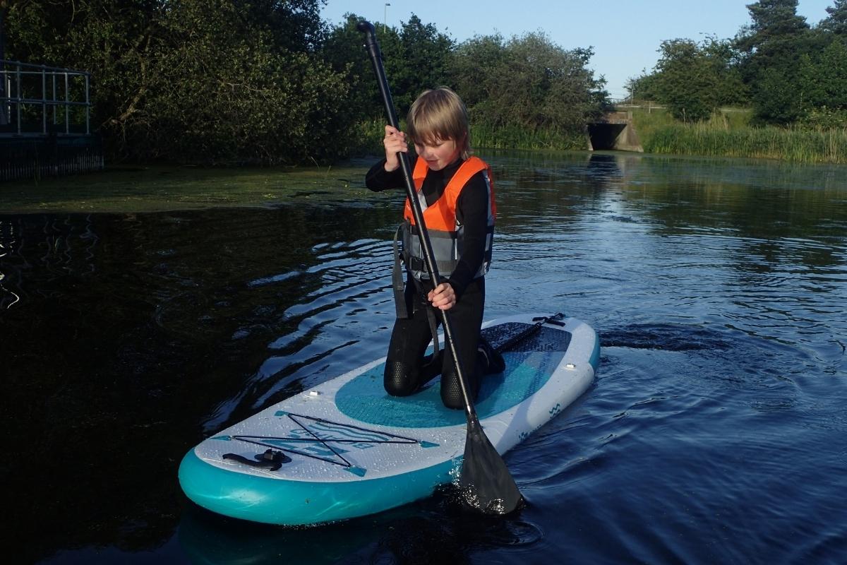 A tween boy kneeling on a EZ Kids paddleboard on a river in the UK